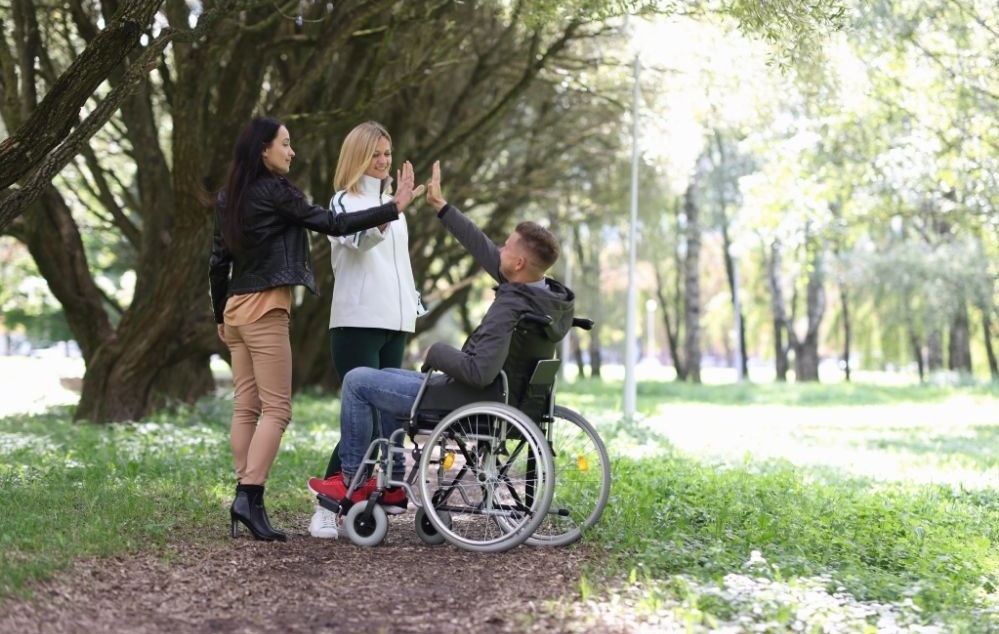 Two friends standing-up high-fiving other friend in wheelchair