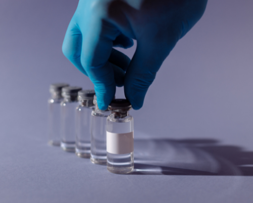 Photo of blue gloved hand lining up vials of a vaccine