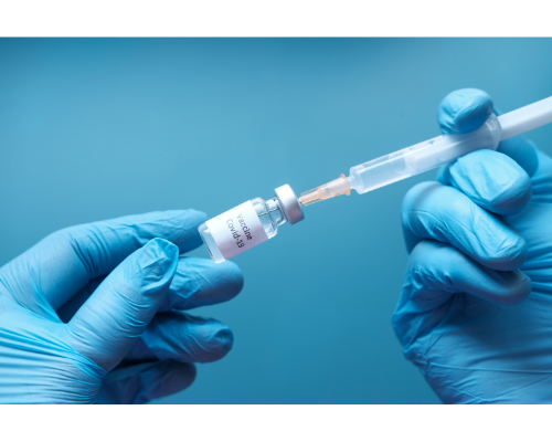 Photo of 2 gloved hands filling a syringe from a vial labeled "COVID-19 vaccine"