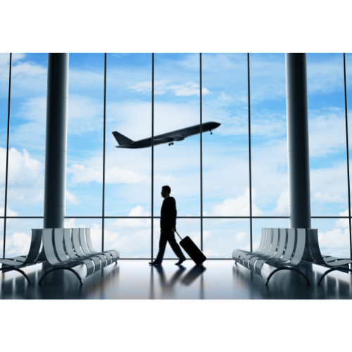 Person with suitcase walking in front of airport window with airplane taking off in background