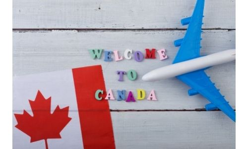 Image of Canadian flag and toy airplane with wooden letters reading "Welcome to Canada"