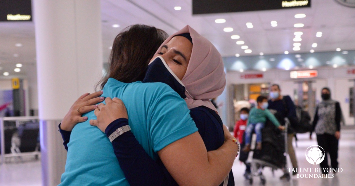 Two people hugging in an airport with Talent Beyond Boundaries logo on photo